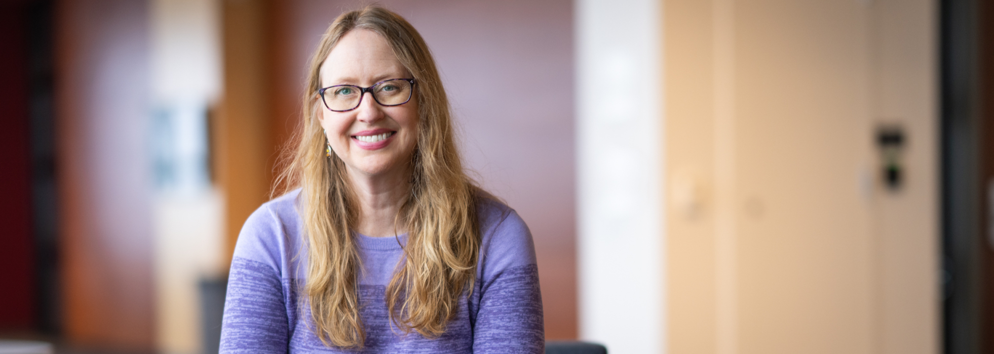 Dr. Amy Zelenski sits near her office wearing a purple sweater