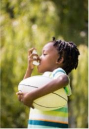 Child with inhaler outside, holding a large white American football.