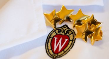 Close-up photo of the UW crest and golden stars on the front of a white lab coat.