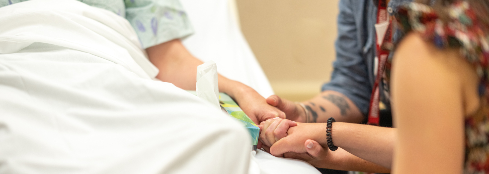 Closeup of patient and companions holding hands at a hospital bedside