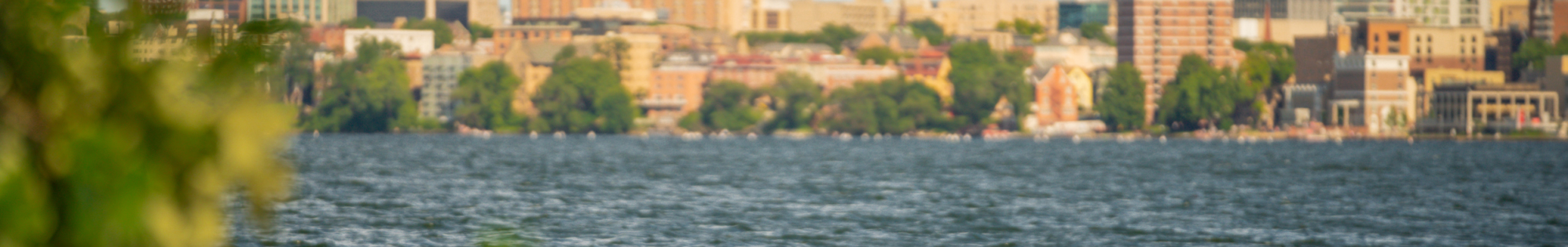 Man on kayak paddling lake Mendota with University of Wisconsin campus and Capitol building in background