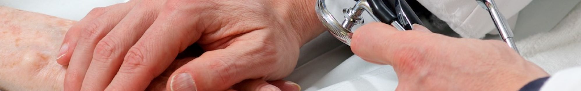 Closeup of physician holding older patient's hand while taking blood pressure