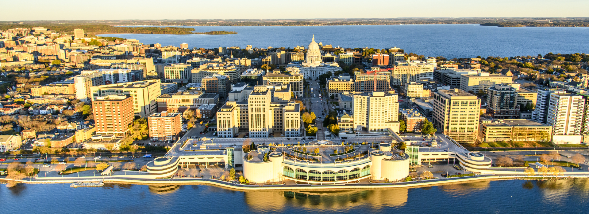 An aerial photo of Madison, with Lake Mendota in the background, the State Capitol and downtown Madison in the mid-ground, and Monona Terrace and Lake Monona in the foreground.