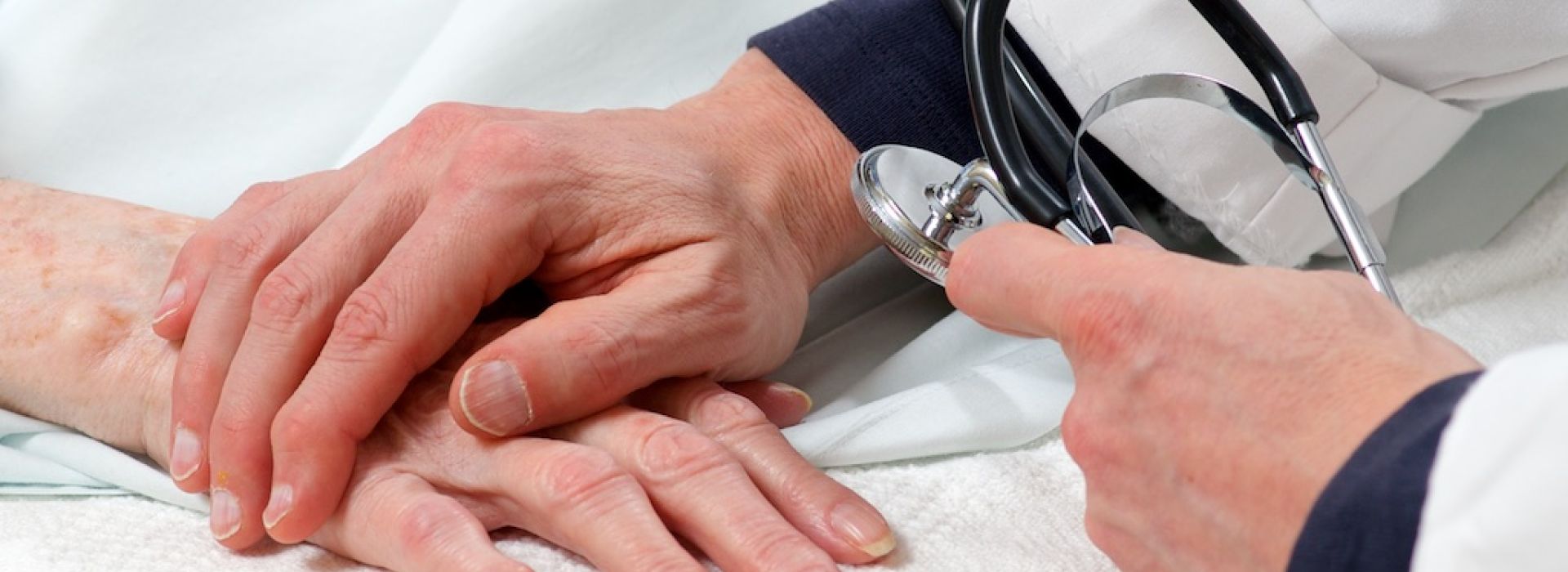 Closeup of physician holding older patient's hand while taking blood pressure