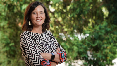 Photo of Carey Gleason, PhD, in front of a background of green leaves.