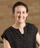 Emily Owen, MD, wears a black shirt with a print and smiles while standing in front of a brick wall