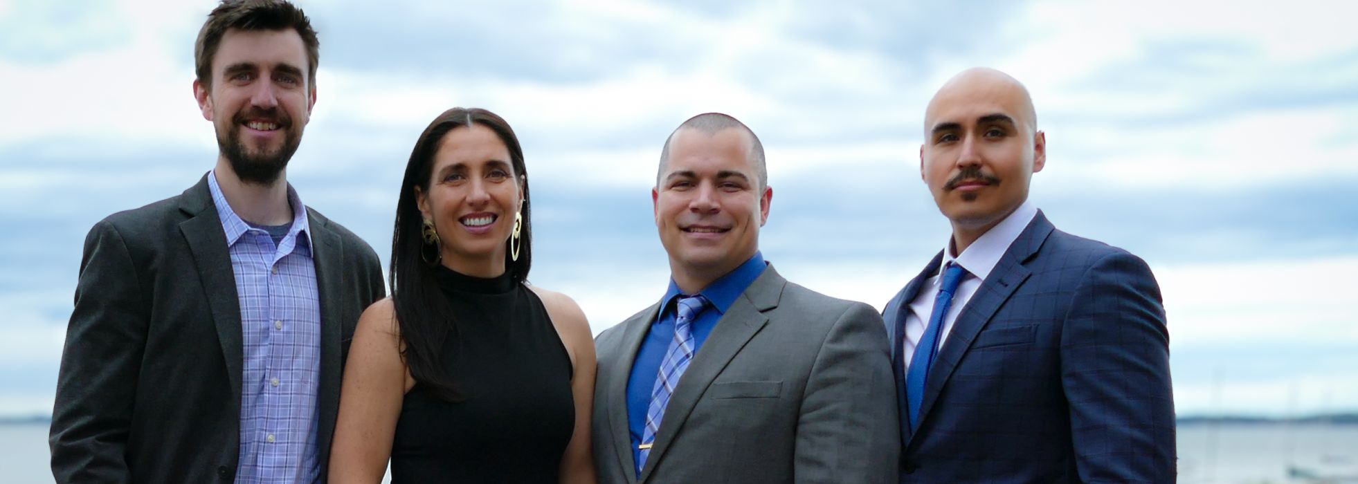 Four people in formal dress standing in a line with a lake in the background