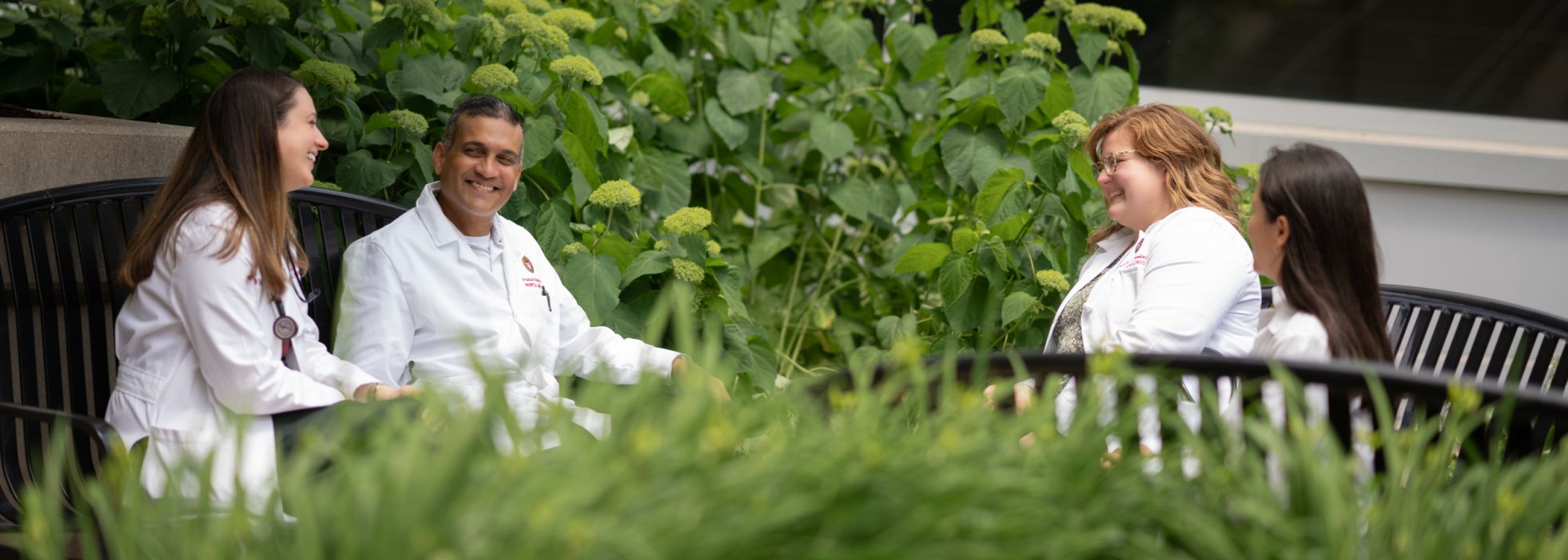 Four doctors in white coats sitting and speaking in a garden