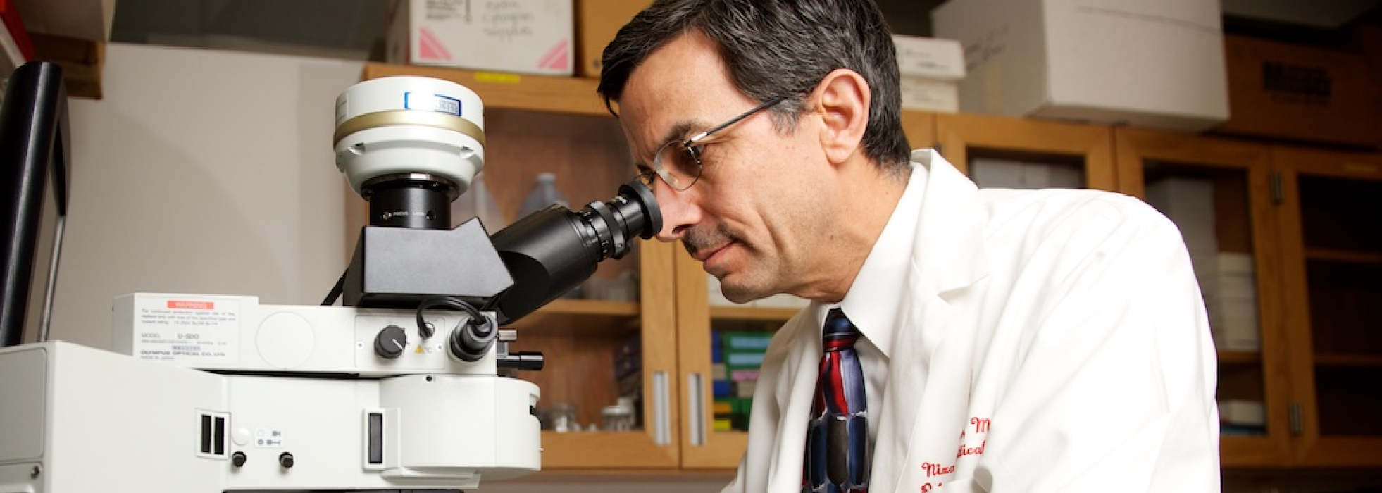 Nizar Jarjour, MD, wearing a white lab coat and looking into a microscope