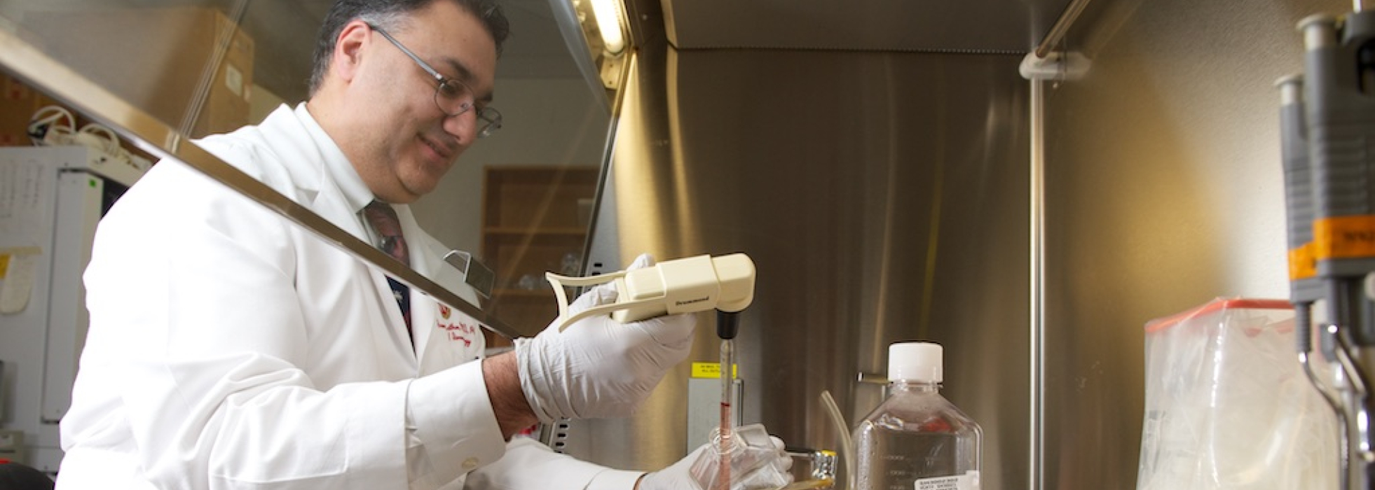 Sameer Mathur, MD, PhD, in a white coat working under a lab hood