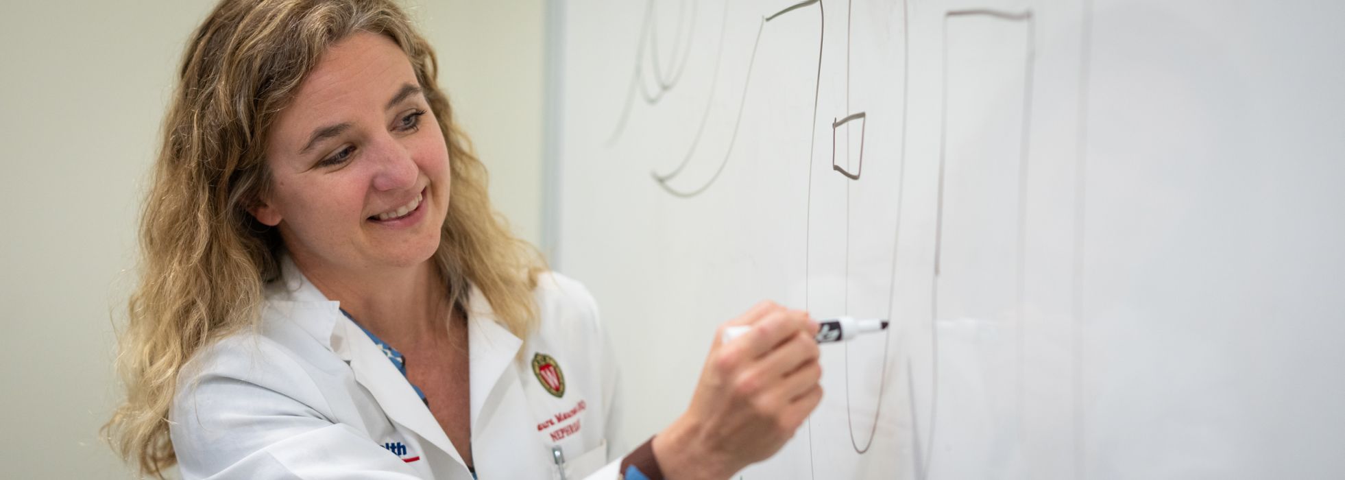 Dr. Laura Maursetter wearing a lab coat and writing on a white board