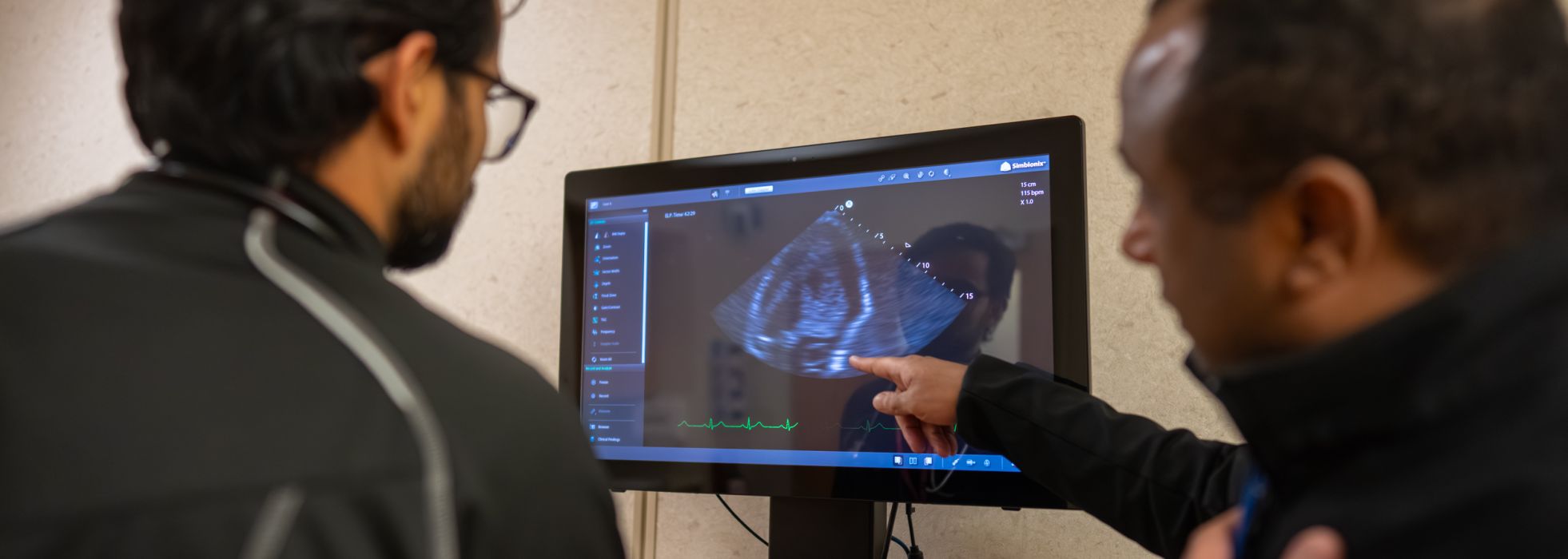 Two men in black jackets looking at an ultrasound, one of them pointing at the screen