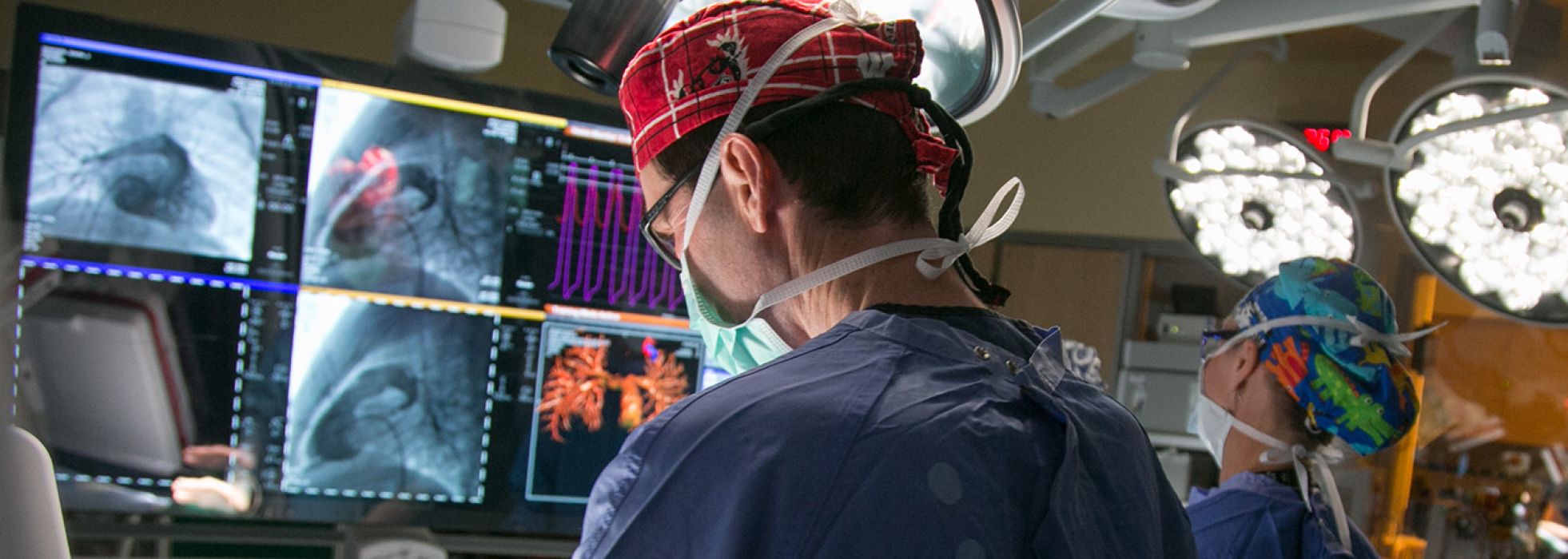 Cardiologist wearing red scrub cap looking at images on a screen in the cath lab