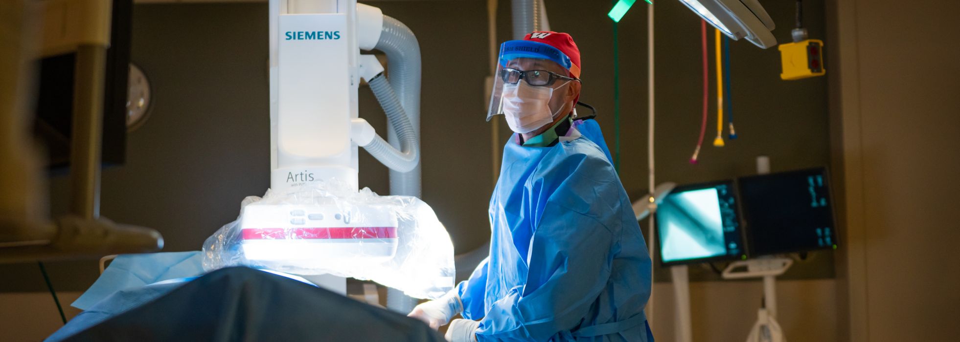 Dr. Micah Chan wearing a red UW scrub cap and face shield performing an interventional nephrology procedure at University Hospital
