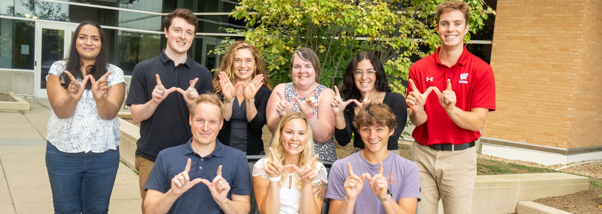 Outdoor photo of Dr. Lee Eckhardt's lab team making "W" sign with hands