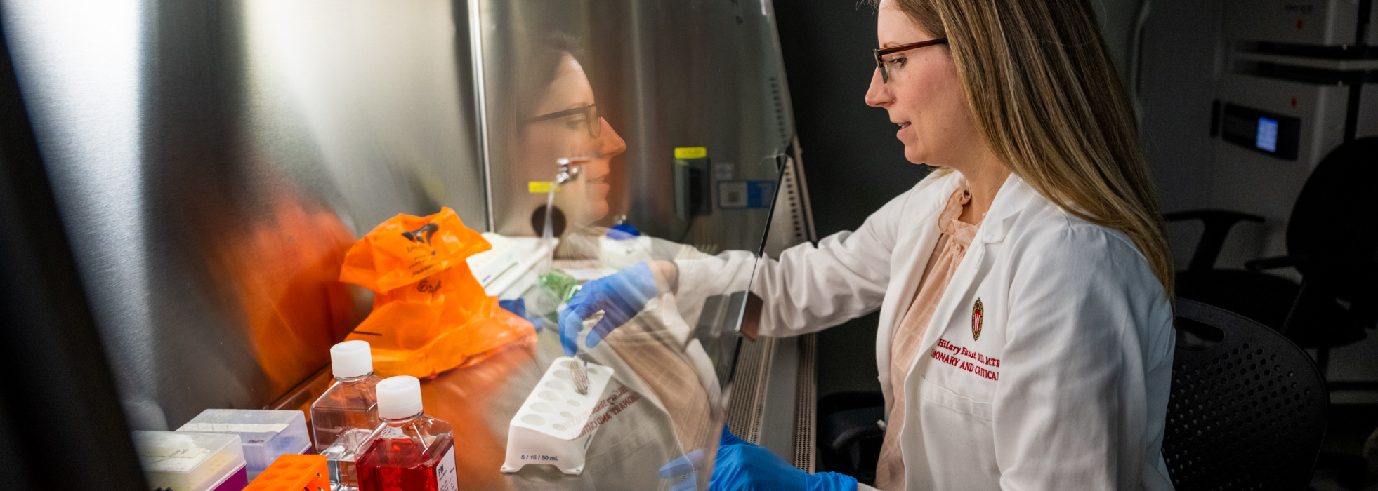 Dr. Hilary Faust in a white coat working under a lab hood