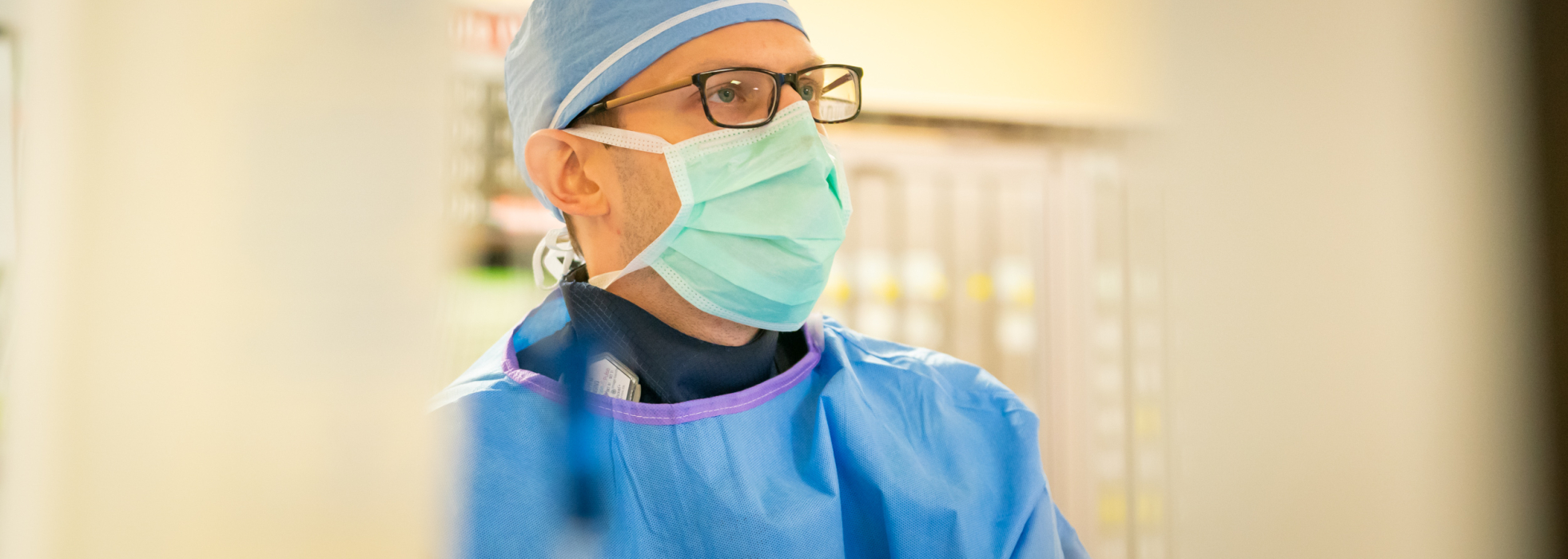 Closeup of cardiovascular medicine fellow wearing a surgical cap, gown and mask working in the cath lab