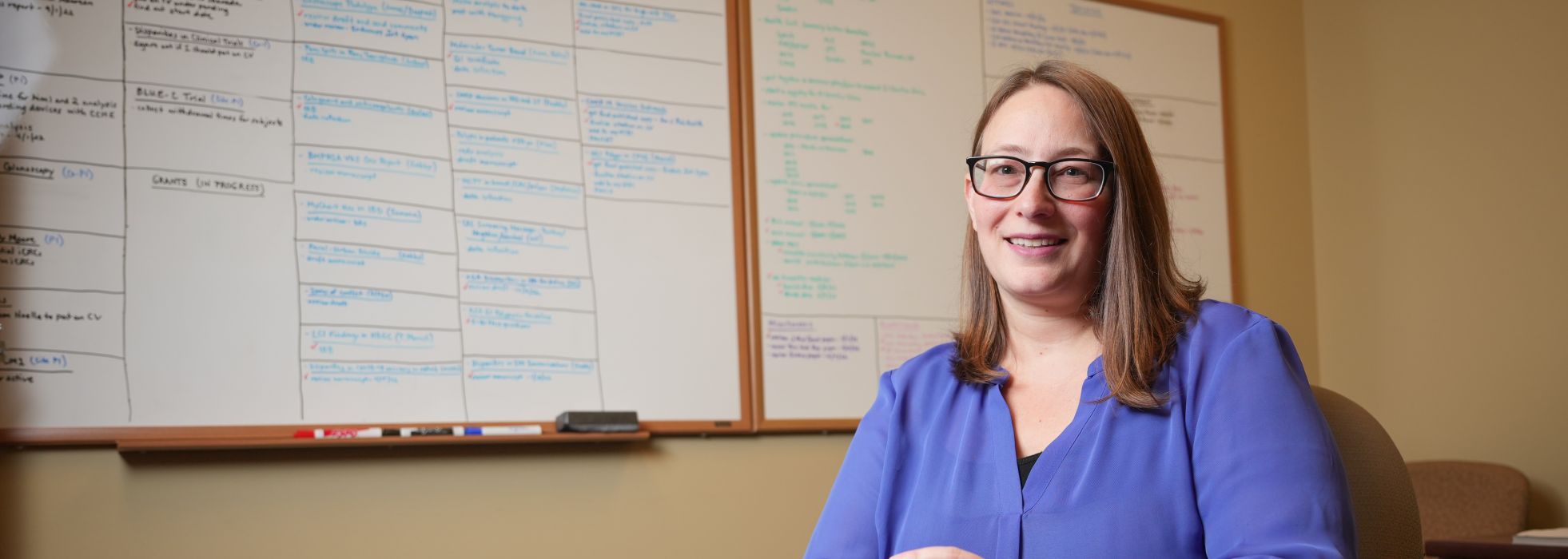 Photo of Dr. Jen Weiss at a table with a whiteboard behind her