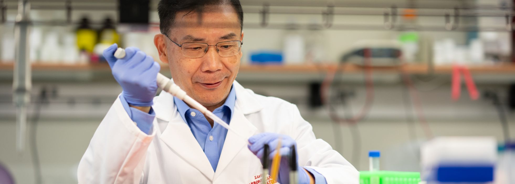 photo of Dr. Lixin Rui wearing a white lab coat and using a pipette at a lab bench