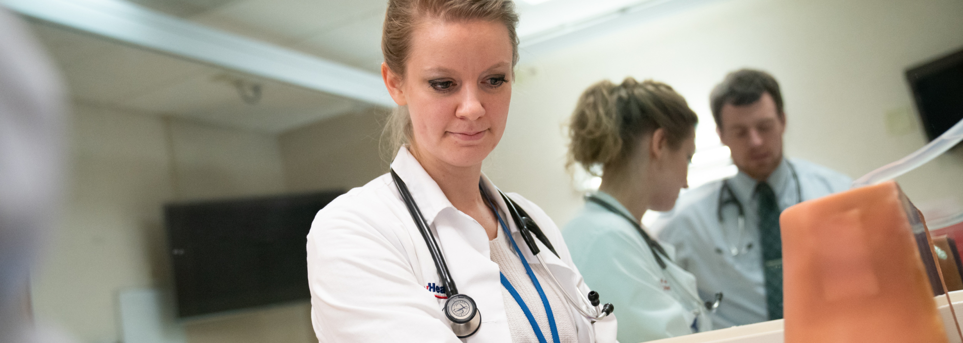 Infectious disease trainee in white coat working in the clinic with colleagues behind her