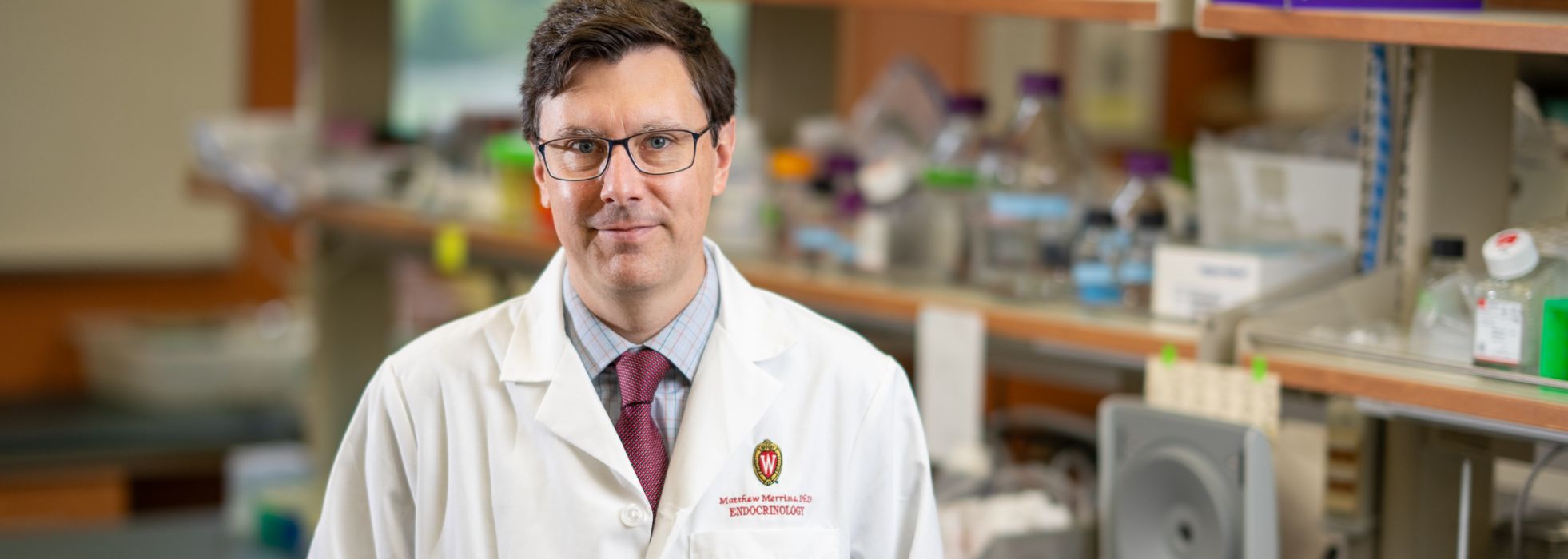 Photo of Dr. Matthew Merrins wearing a white lab coat in his lab