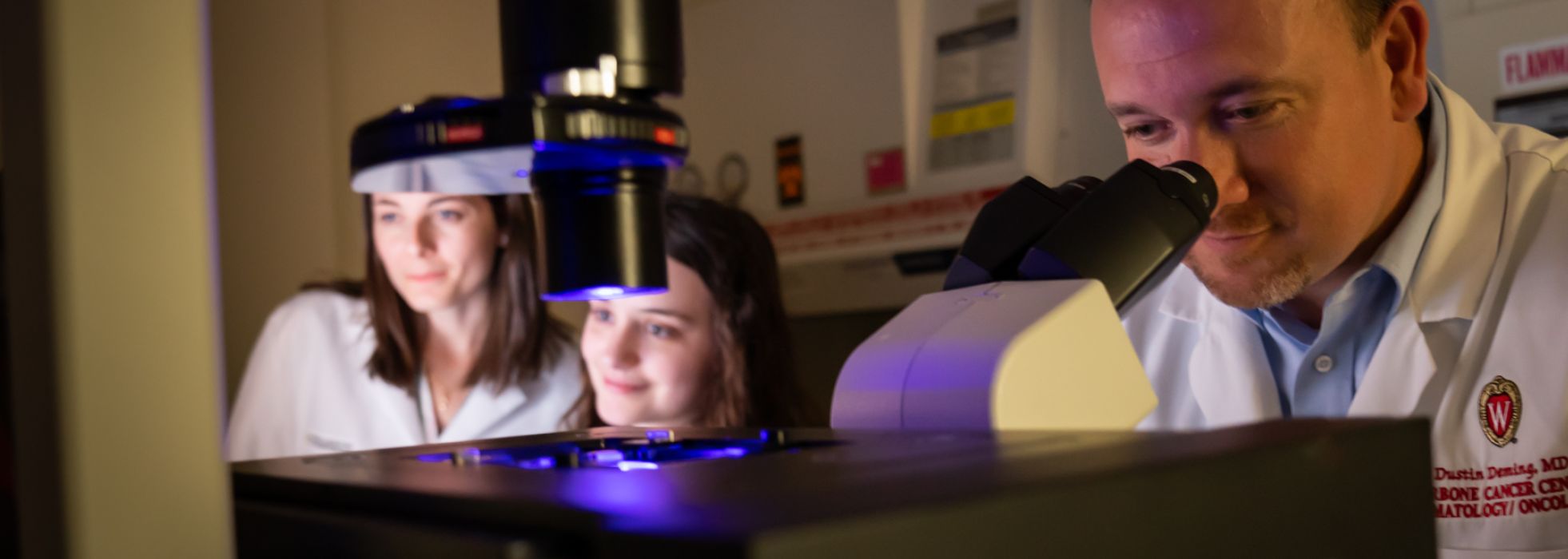 photo of Dr. Dusty Deming and others in lab looking at microscope