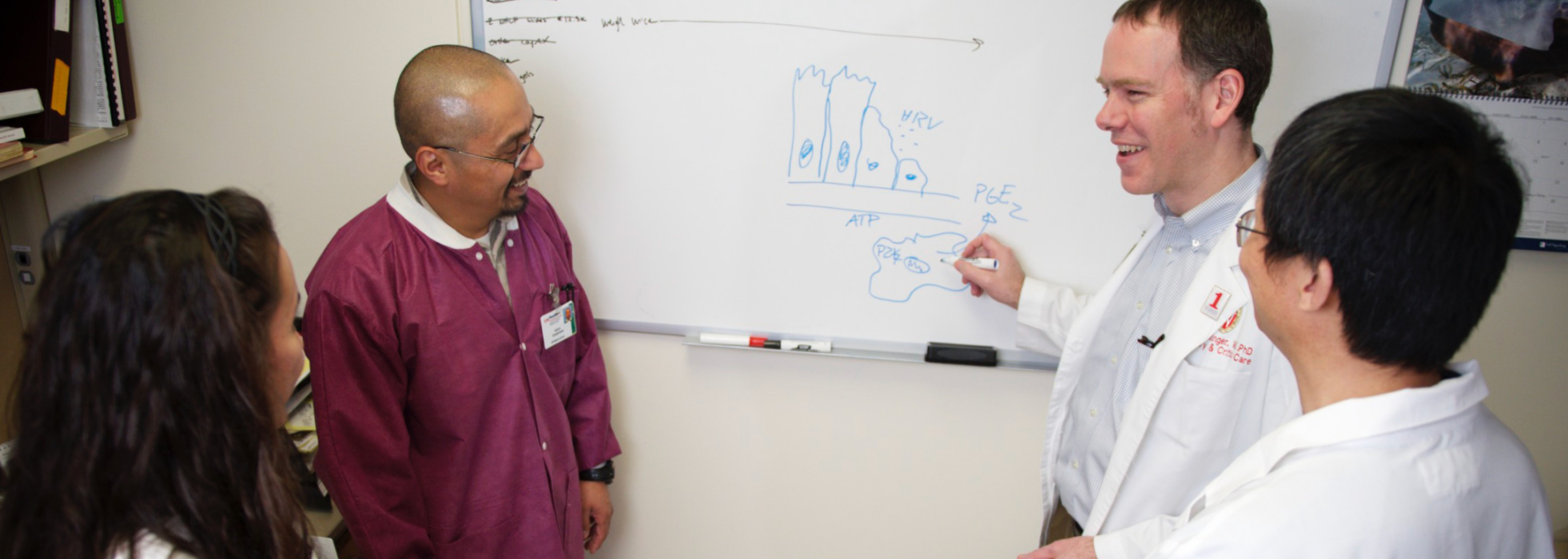 Dr. Loren Denlinger lectures to three trainees in front of a whilteboard