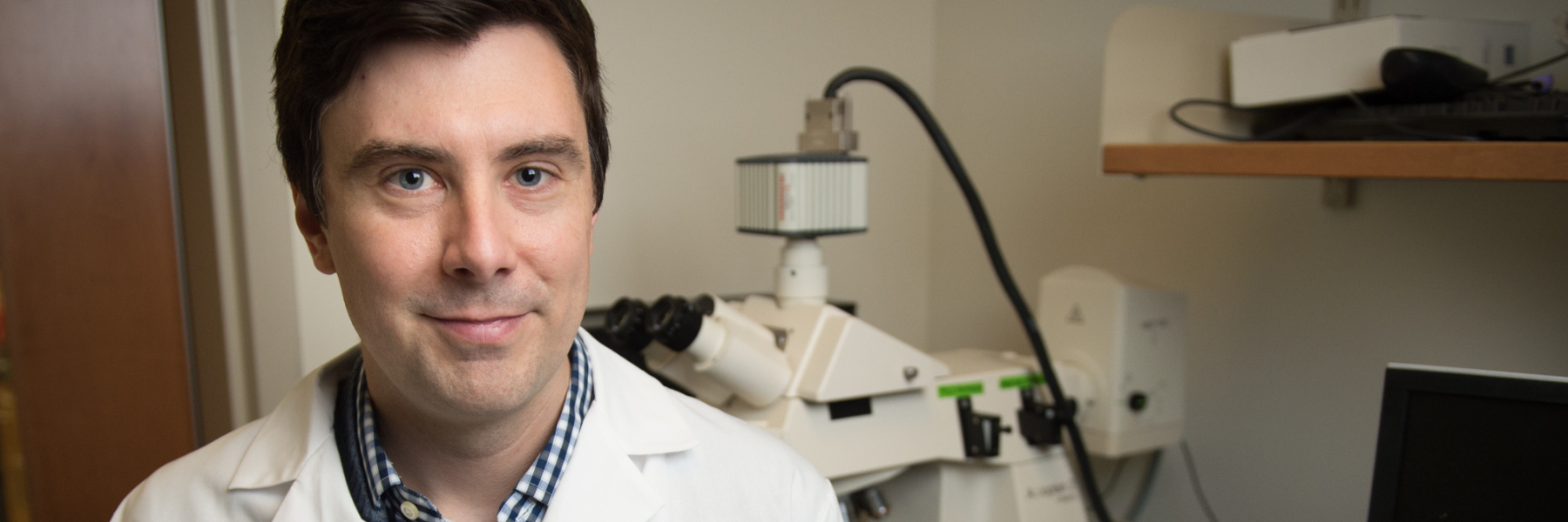 Photo of Dr. Matthew Merrins wearing a white lab coat in his lab