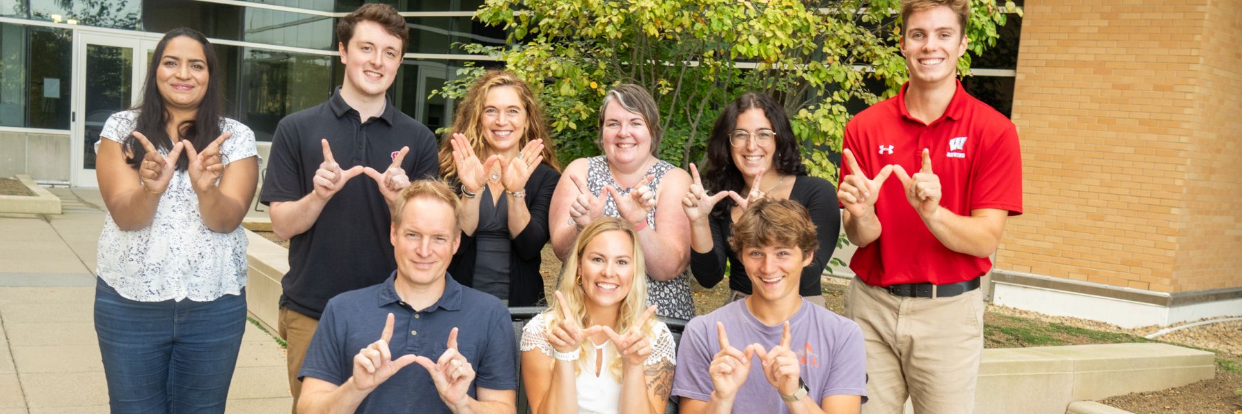 Outdoor photo of Dr. Lee Eckhardt's lab team making "W" sign with hands