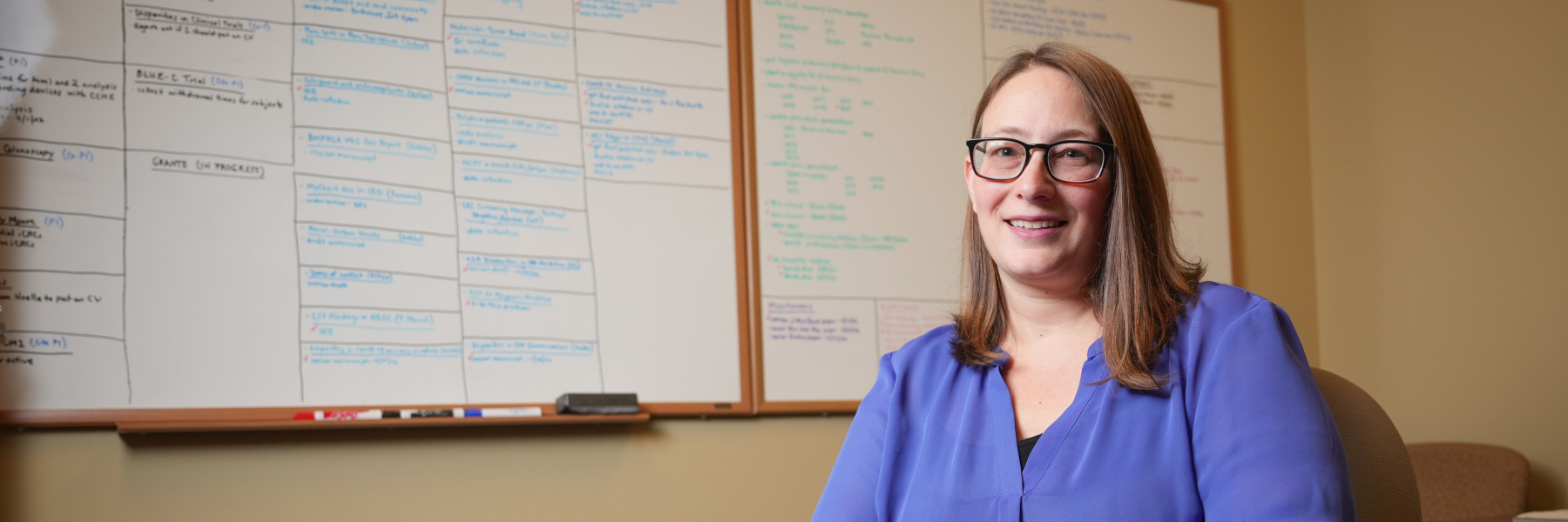 photo of Dr. Jen Weiss at a table with a whiteboard behind her