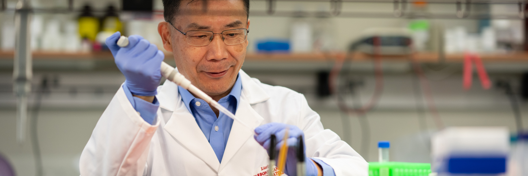 photo of Dr. Lixin Rui wearing a white lab coat and using a pipette at a lab bench