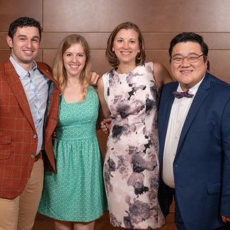 Dr. Murray-Bainer wears a black and white print dress and stands in the middle of a small group of her fellow graduating chief residents.