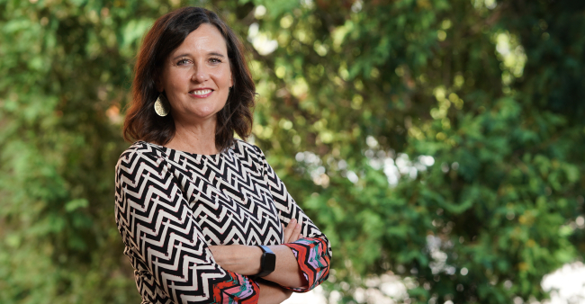 Photo of Carey Gleason, PhD, in front of a background of green leaves.