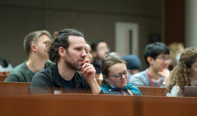 DOM learners watch Dr. Reeni Abraham’s Grand Rounds in an auditorium.