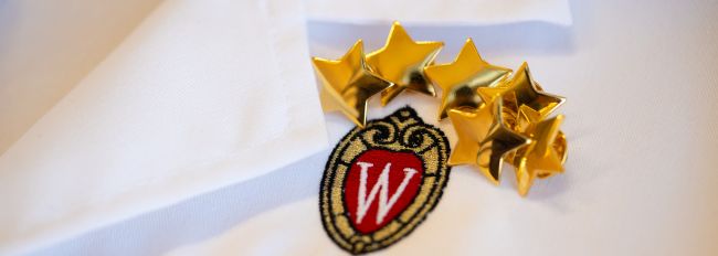 Close-up photo of the UW crest and golden stars on the front of a white lab coat.