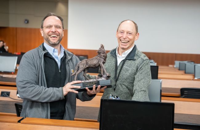 James Lewallen and Steve Barczi stand in an auditorium holding a wolf trophy
