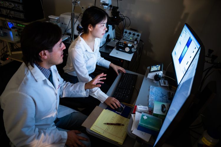photo of Dr. Francisco Alvarado and member of lab team in front of computer screens in darkened lab