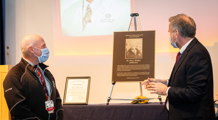 Dr. Alan Bridges, on left, facing Madison VA director John Rohrer, MPH, at the unveiling of the commemorative plaque that will hang outside the newly-named Alan J. Bridges Auditorium at the Madison VA..