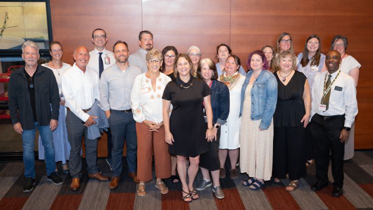 Sheri Lawrence (center) smiles with nearly 20 of her current and former direct reports at a recent gathering to celebrate her retirement. 
