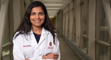 Dr. Shivani Garg in her white coat, standing in a hallway.