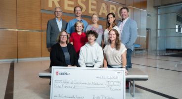 Photo of some of the Dotzauer family and friends, with Heather Dotzauer at lower right, gathered for a check presentation with Dr. Hector Valdivia, at top left, representing the Division of Cardiovascular Medicine.