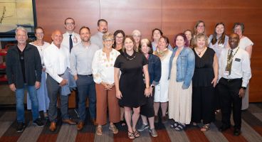 Sheri Lawrence (center) smiles with nearly 20 of her current and former direct reports at a recent gathering to celebrate her retirement. 