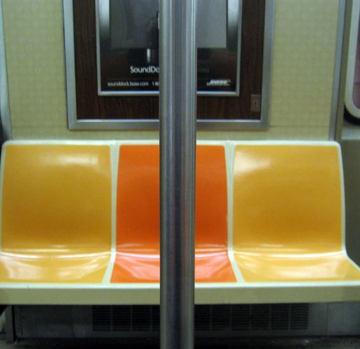Empty orange and yellow seats in a New York City subway car.