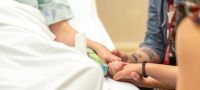 Patient in hospital bed, holding hands with loved ones.