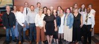 Sheri Lawrence (center) smiles with nearly 20 of her current and former direct reports at a recent gathering to celebrate her retirement. 