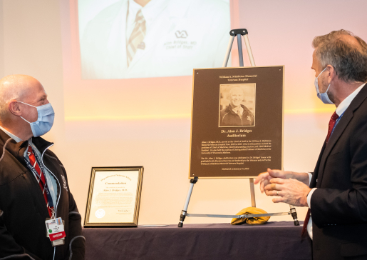 Dr. Alan Bridges, on left, facing Madison VA director John Rohrer, MPH, at the unveiling of the commemorative plaque that will hang outside the newly-named Alan J. Bridges Auditorium at the Madison VA..