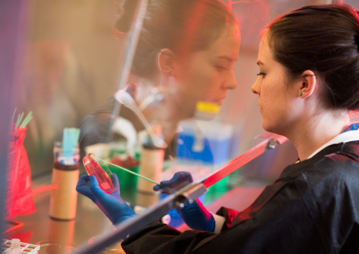 Infectious disease researcher sampling a petri dish with her reflection in the lab hood