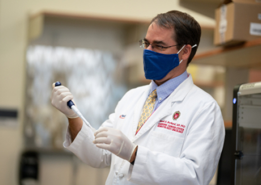 Dr. Mark Burkard wearing a mask and white lab coat holding a pipette