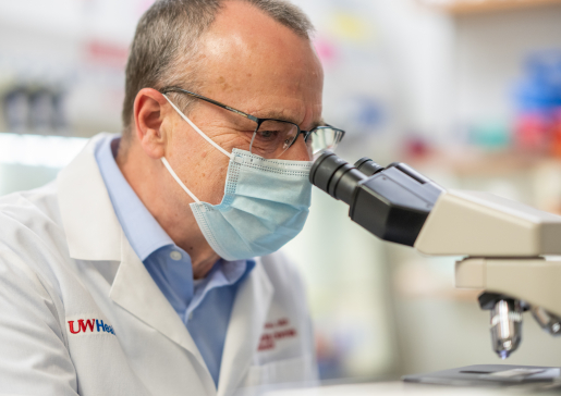 Dr. Mark Albertini wearing a mask looking into a microscope