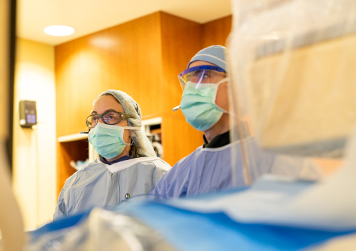 Two cardiologists in masks, caps and gowns working in the cath lab